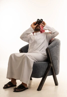 Saudi Man Using Binoculars on Gray Chair White Background