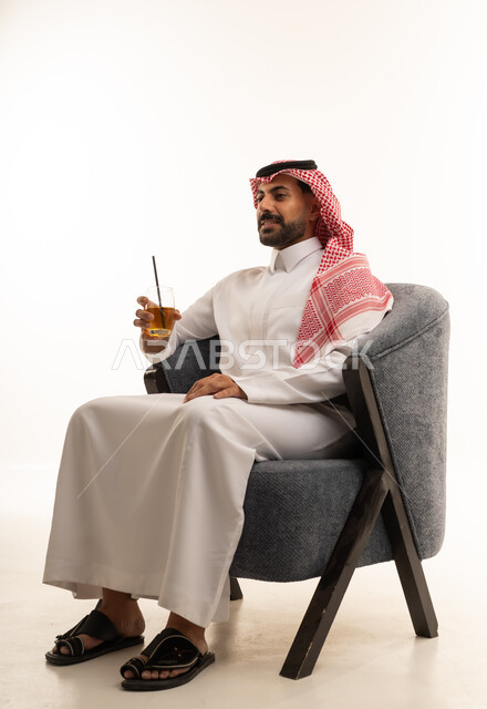 رجل سعودي بالزي التقليدي يجلس على كرسي رمادي