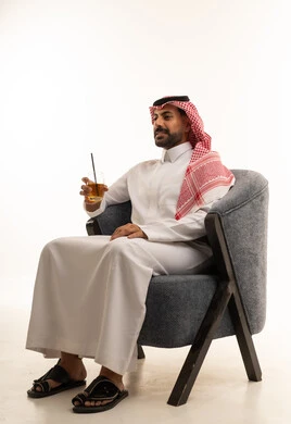 رجل سعودي بالزي التقليدي يجلس على كرسي رمادي