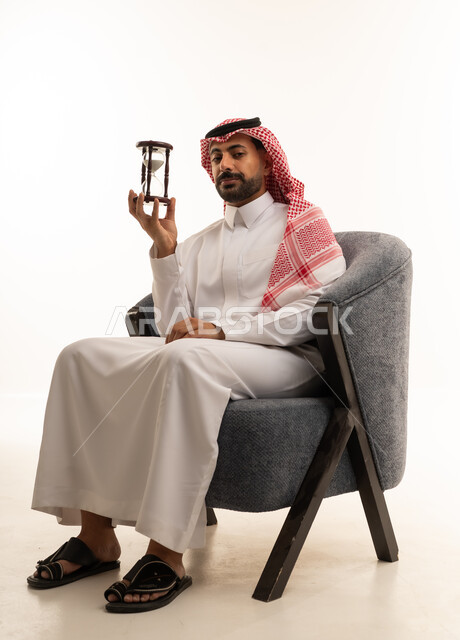 رجل سعودي بالزي التقليدي يمسك ساعة رملية