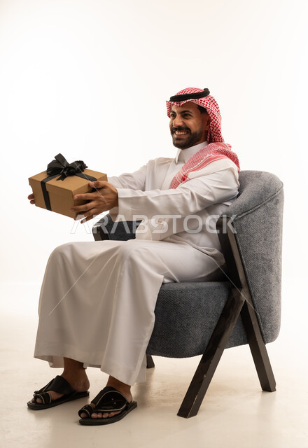 رجل سعودي بالزي التقليدي يمسك صندوق هدايا
