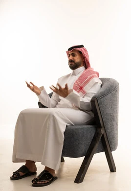 رجل سعودي بالزي التقليدي يجلس ويشير بيديه بحيرة