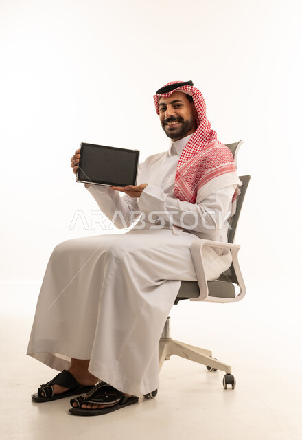 رجل أعمال سعودي يحمل جهاز لوحي على كرسي مكتب