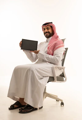 رجل أعمال سعودي يحمل جهاز لوحي على كرسي مكتب