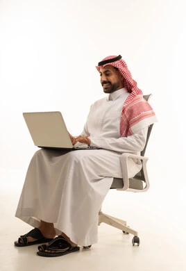 رجل سعودي يستخدم اللابتوب على كرسي مكتب خلفية بيضاء