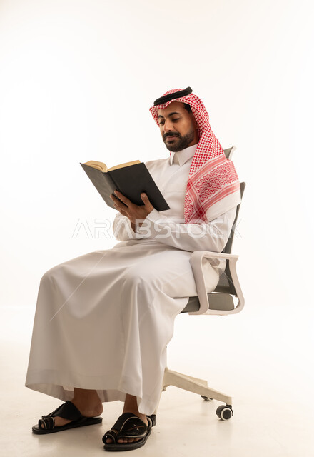 رجل سعودي بالزي التقليدي يقرأ كتاباً في الاستوديو