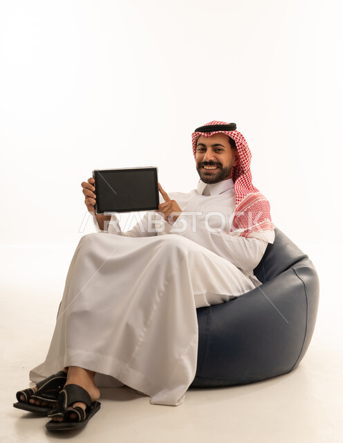 رجل سعودي يحمل جهاز لوحي على مقعد مريح