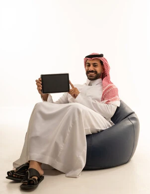 رجل سعودي يحمل جهاز لوحي على مقعد مريح