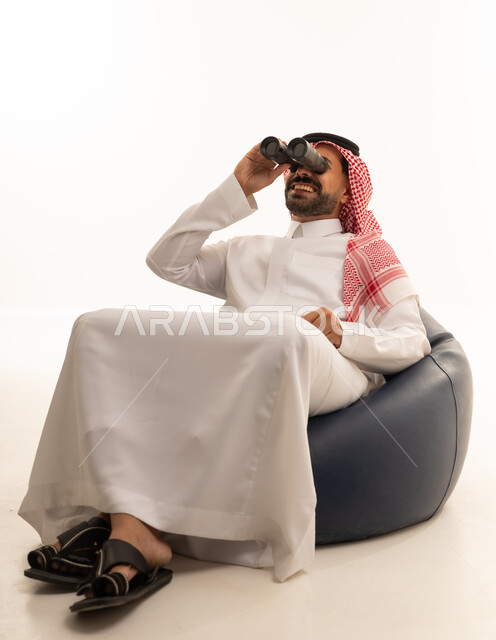 رجل سعودي بالثوب التقليدي يستخدم المنظار