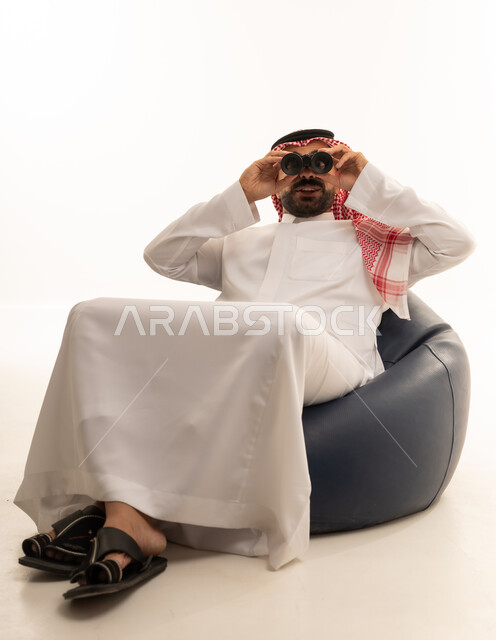 رجل سعودي بالثوب التقليدي يستخدم المنظار بخلفية بيضاء