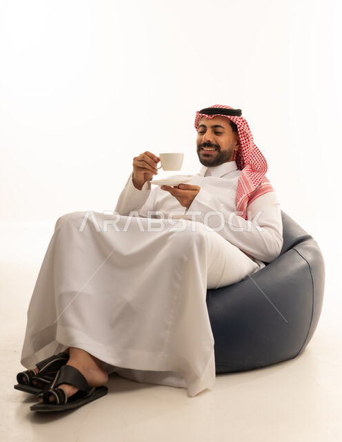 رجل سعودي بالزي التقليدي يشرب القهوة على كرسي استرخاء