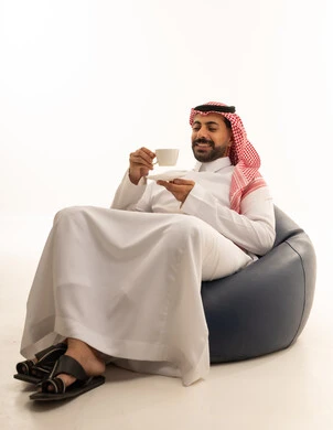 رجل سعودي بالزي التقليدي يشرب القهوة على كرسي استرخاء