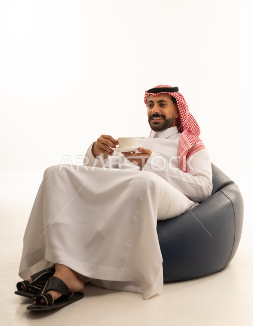 رجل سعودي بالثوب التقليدي يجلس مع كوب قهوة