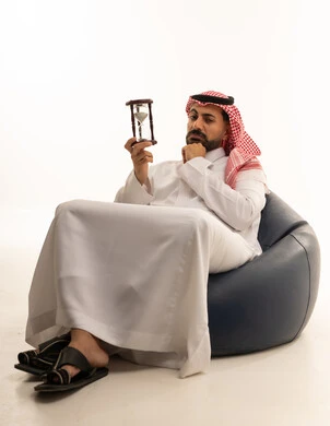 رجل سعودي بالثوب والشماغ يحمل ساعة رملية