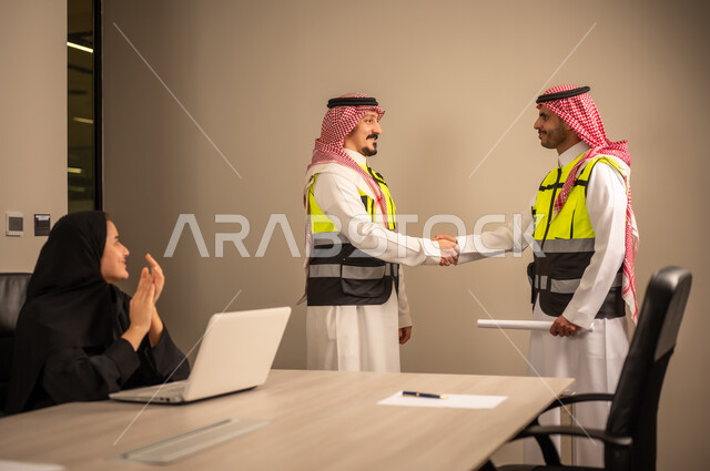 العمل في القطاع الهندسي، متابعة مخطط الاعمار,مفهوم الهندسة والانشاءات المعمارية، مهندسة عربية خليجية سعودية تصفق بايديها وامامها جهاز اللابتوب ، مهندسان عربيان خليجيان سعوديان يرتديان الثوب التقليدي والشماغ وسترة الحماية يتصافحان ويقيما اتفاق ، مهنة ووظيفة في السعودية