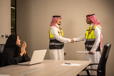 العمل في القطاع الهندسي، متابعة مخطط الاعمار,مفهوم الهندسة والانشاءات المعمارية، مهندسة عربية خليجية سعودية تصفق بايديها وامامها جهاز اللابتوب ، مهندسان عربيان خليجيان سعوديان يرتديان الثوب التقليدي والشماغ وسترة الحماية يتصافحان ويقيما اتفاق ، مهنة ووظيفة في السعودية
