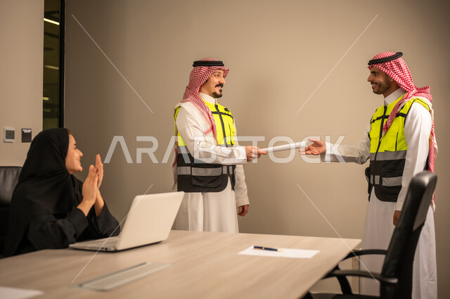 العمل في القطاع الهندسي، متابعة مخطط الاعمار,مفهوم الهندسة والانشاءات المعمارية، مهندسة عربية خليجية سعودية تصفق بايديها وامامها جهاز اللابتوب ، مهندس عربي خليجي سعودي يرتدي الثوب التقليدي والشماغ وسترة الحماية يسلم مخطط هندسي لمهندس معماري ، مهنة ووظيفة في السعودية