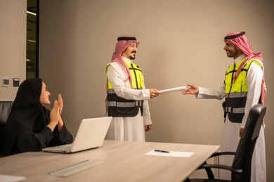 العمل في القطاع الهندسي، متابعة مخطط الاعمار,مفهوم الهندسة والانشاءات المعمارية، مهندسة عربية خليجية سعودية تصفق بايديها وامامها جهاز اللابتوب ، مهندس عربي خليجي سعودي يرتدي الثوب التقليدي والشماغ وسترة الحماية يسلم مخطط هندسي لمهندس معماري ، مهنة ووظيفة في السعودية