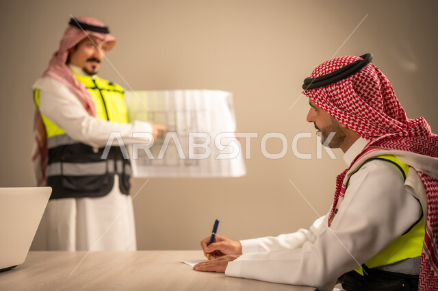 العمل في القطاع الهندسي، متابعة مخطط الاعمار,مفهوم الهندسة والانشاءات المعمارية، مهندس عربي خليجي سعودي يرتدي الثوب التقليدي والشماغ وسترة الحماية يمسك بيده المخطط يتناقش مع مهندس معماري  ، مهنة ووظيفة في السعودية