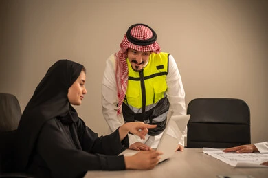 دمج التقنيات المتطورة فى العمل، مفهوم الهندسة والانشاءات المعمارية،  العمل في القطاع الهندسي، متابعة مخطط الاعمار, مهندسة عربية خليجية سعودية ترتدي العباءة والحجاب تستخدم جهاز اللابتوب وتتناقش مع مهندس معماري ، مهنة ووظيفة في السعودية