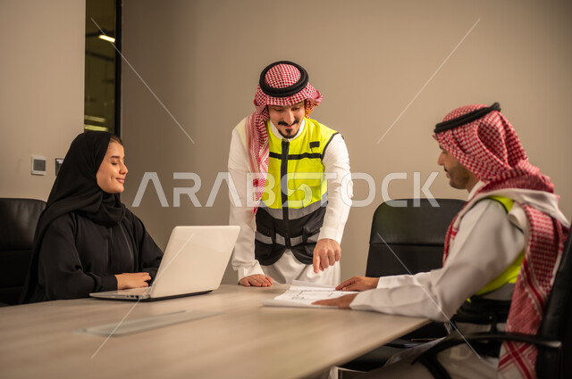 دراسة الرسوم البيانية والاحصاءات، متابعة مخطط الاعمار, العمل في القطاع الهندسي، مفهوم الهندسة والانشاءات المعمارية، مهندس عربي خليجي سعودي يرتدي الثوب التقليدي والشماغ وسترة الحماية يمسك بيده المخطط يجلس مع موظفة تمسك بيدها جهاز اللابتوب ومهندس معماري  ، مهنة ووظيفة في السعودية