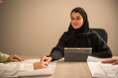 دراسة الرسوم البيانية والاحصاءات، متابعة مخطط الاعمار, العمل في القطاع الهندسي، مفهوم الهندسة والانشاءات المعمارية، موظفة سعودية تمسك بيدها جهاز التابلت تتناقش مع مهندسين عربيين خليجيين سعوديين يرتديون الثوب التقليدي والشماغ وسترة الحماية امامهم المخطط  ، مهنة ووظيفة في السعودية