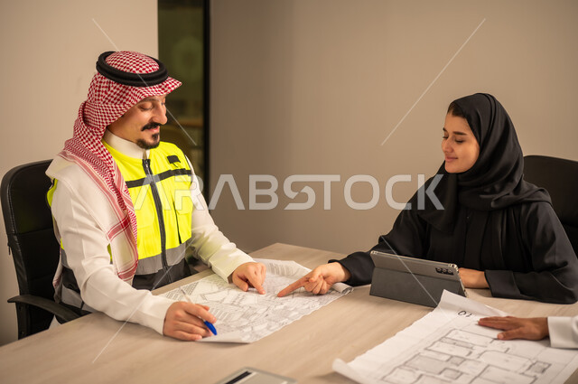 دراسة الرسوم البيانية والاحصاءات، متابعة مخطط الاعمار, العمل في القطاع الهندسي، مفهوم الهندسة والانشاءات المعمارية، موظفة سعودية تمسك بيدها جهاز التابلت تتناقش مع مهندسين عربيين خليجيين سعوديين يرتديون الثوب التقليدي والشماغ وسترة الحماية امامهم المخطط  ، مهنة ووظيفة في السعودية