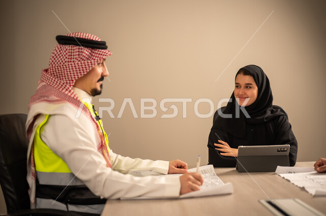 دراسة الرسوم البيانية والاحصاءات، متابعة مخطط الاعمار, العمل في القطاع الهندسي، مفهوم الهندسة والانشاءات المعمارية، مهندس عربي خليجي سعودي يرتدي الثوب التقليدي والشماغ وسترة الحماية يمسك بيده المخطط يجلس مع موظفة تمسك بيدها جهاز التابلت ، مهنة ووظيفة في السعودية