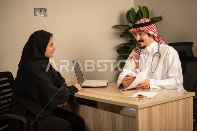 Project and investment development, studying working papers, using a laptop, two Arab Gulf Saudi employees conducting a business meeting inside the office, integrating modern technology with office work, managing and dividing tasks.