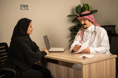 Project and investment development, studying working papers, using a laptop, two Arab Gulf Saudi employees conducting a business meeting inside the office, integrating modern technology with office work, managing and dividing tasks.