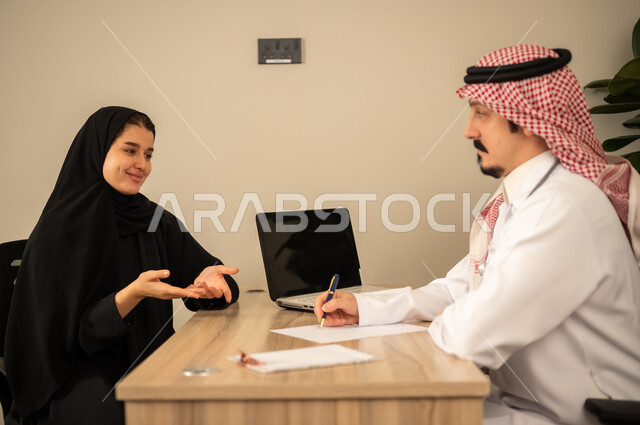 Project and investment development, studying working papers, using a laptop, two Arab Gulf Saudi employees conducting a business meeting inside the office, integrating modern technology with office work, managing and dividing tasks.