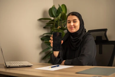 عرض شاشة سوداء فارغة، مهن وأعمال مكتبية، استخدام الهاتف المحمول، توفير بيئة عمل مريحة ومناسبة، استعمال جهاز الحاسوب المحمول لإنجاز المهام باحترافية، امراه عربية خليجية سعودية ترتدي العباءة السوداء والحجاب  تجلس في المكتب تقوم بالعمل عبر اللابتوب، التوظيف في المكاتب والشركات السعودية