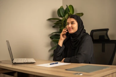 Writing and documenting reports, office jobs and tasks, using mobile phones, providing a comfortable and suitable work environment, using a laptop to complete tasks professionally, an Arab Gulf Saudi man wearing traditional thobe and ghutrah sitting in the office working on a laptop, employment in Saudi offices and companies.