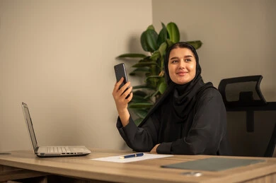 Writing and documenting reports, office jobs and tasks, using mobile phones, providing a comfortable and suitable work environment, using a laptop to complete tasks professionally, an Arab Gulf Saudi man wearing traditional thobe and ghutrah sitting in the office working on a laptop, employment in Saudi offices and companies.
