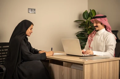 دراسة أوراق العمل, استخدام الحاسوب المحمول، موظفان عربيان خليجيان سعوديان يقومان بإجراء اجتماع عمل داخل غرفة الاجتماعات في مقر الشركة، دمج الأجهزة التقنية الحديثة بالأعمال المكتبية، تطوير المشاريع و الاستثمارات, إدارة و تقسيم المهام