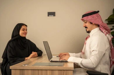 Two Saudi Arabian Gulf Arab employees are holding a business meeting inside the conference room at the company's headquarters, reviewing work papers, using a laptop, integrating modern technological devices with office work, developing projects and investments, managing and dividing tasks. Two Saudi Arabian Gulf Arab employees are holding a business meeting inside the conference room at the company's headquarters, reviewing work papers, using a laptop, integrating modern technological devices with office work, developing projects and investments, managing and dividing tasks.
