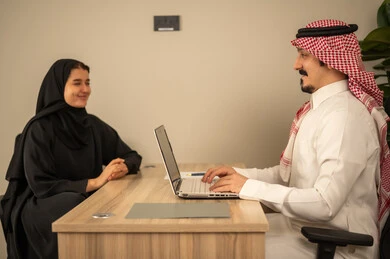 Study of working papers, use of laptops, two Arab Gulf Saudi employees conducting a business meeting inside the company's conference room, integrating modern technology with office work, developing projects and investments, managing and dividing tasks. Study of working papers, use of laptops, two Arab Gulf Saudi employees conducting a business meeting inside the company's conference room, integrating modern technology with office work, developing projects and investments, managing and dividing tasks.