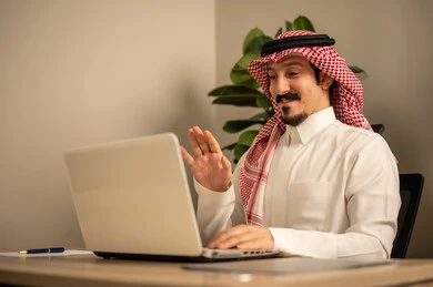 Providing a comfortable and suitable work environment, employment in Saudi offices and companies, using a laptop to complete tasks professionally, an Arab Gulf Saudi man wearing traditional thobe and ghutrah working on a laptop inside the office.