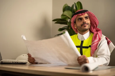 Development and evolution of work in the engineering field, architectural designs and plan verification, a Saudi Gulf Arab engineer wearing a safety coat holding a work plan, management of engineering projects, Saudi professions and jobs. Development and evolution of work in the engineering field, architectural designs and plan verification, a Saudi Gulf Arab engineer wearing a safety coat holding a work plan, management of engineering projects, Saudi professions and jobs.