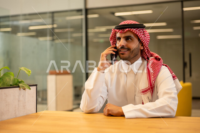 إيماءات الجودة والرضا والقبول, العمل في المجال المكتبي,رجل عربي خليجي سعودي مبتسم يرتدي الثوب التقليدي والشماغ يقوم بإجراء مكالمة هاتفية عبر الهاتف المحمول,متابعه الأعمال الادارية