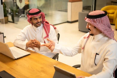 Integrating work with advanced technology, two Arab Gulf Saudi employees wearing traditional thob and ghutrah are using modern technical devices, Saudi professions and jobs, achieving the company's goals, the Saudi work environment.