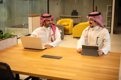 مناقشة وإنجاز مهام العمل ،دمج العمل مع التكنولوجيا المتطورة، موظفان عربيان خليجيان سعوديان يرتديان الثوب التقليد والشماغ يستخدمان الاجهزة التقنية الحديثة، مهن ووظائف سعودية، تحقيق أهداف الشركة، بيئة العمل السعودي.