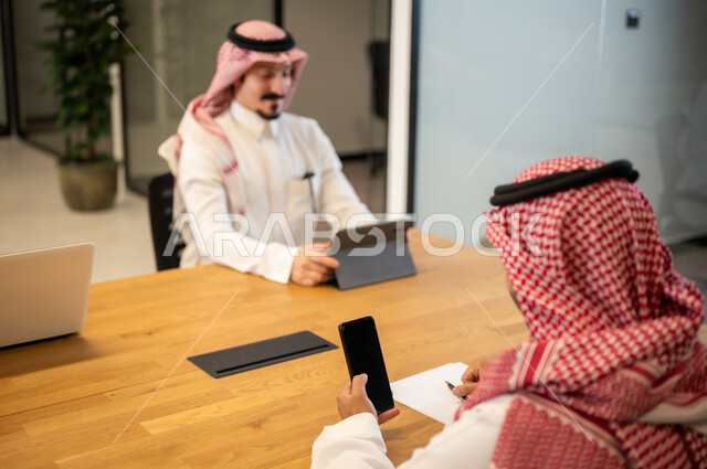 The Saudi work environment, integrating work with advanced technology, Arab Gulf Saudi employees using modern technical devices, accomplishing work tasks, Saudi professions and jobs, achieving the company's goals.