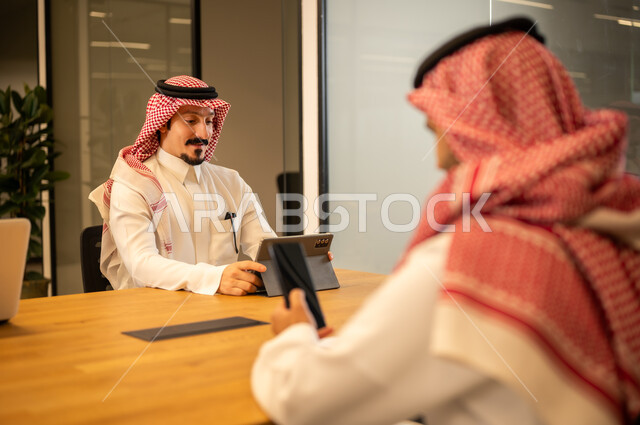 Integrating work with advanced technology, Arab Gulf Saudi employees using modern technical devices, accomplishing work tasks, Saudi professions and jobs, achieving company goals, the Saudi work environment.