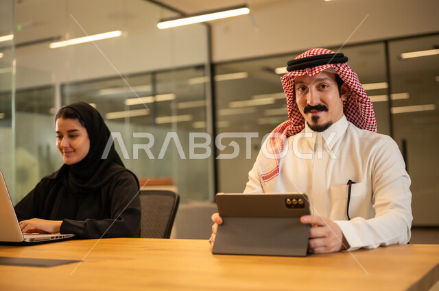 موظفين عربيين خليجيين سعوديين يستخدمون الاجهزة التقنية الحديثة، إنجاز مهام العمل ،مهن ووظائف سعودية، تحقيق أهداف الشركة، دمج العمل مع التكنولوجيا المتطورة، بيئة العمل السعودي.