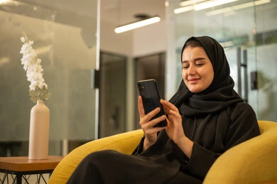 Follow-up of administrative work, gestures of quality, satisfaction, and acceptance, a Saudi Arabian Gulf woman wearing a black abaya using a mobile phone, working in the office field.
