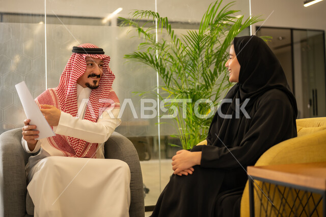 الإشارة الى العقود و الاشراف على التطور المهني، مفهوم الإدارة المتعاونة لتحقيق أهداف الشركة، موظفين عربيين خليجيين سعوديين يتناقشان في أمور العمل باستخدام الأوراق،التعاون والتفاعل الجماعي و حل المشكلات