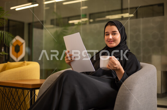 اعداد التقارير الخاصة بالعمل، التدقيق في قراءة الملاحظات،امرأة عربية سعودية خليجية محجبة ترتدي العباءة السوداء تحمل بيدها مجموعة من الاوراق البيضاء، مراجعة ومتابعة الخطط والمشاريع المكتبية بإيماءات التركيز