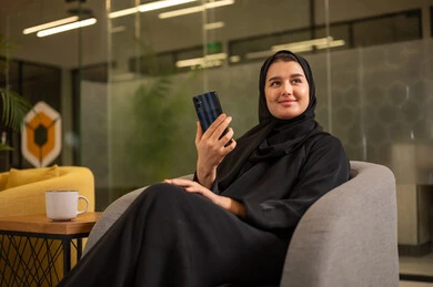 Gestures of quality, satisfaction, and acceptance, a Saudi Arabian Gulf woman wearing a black abaya is making a phone call on her mobile phone, working in the office field, following up on administrative tasks.