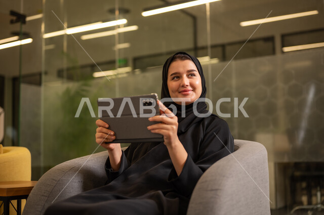 دمج التقنيات الحديثة بالمجال الإداري والمكتبي، شركات ومكاتب خليجية في السعودية, جلسه عمل عن بعد، امرأة عربية سعودية خليجية محجبة ترتدي العباءة السوداء تستخدم جهاز التابلت